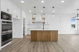 Kitchen featuring stainless steel double oven, a kitchen island with sink, two tone cabinets, light wood finished floors, and black microwave