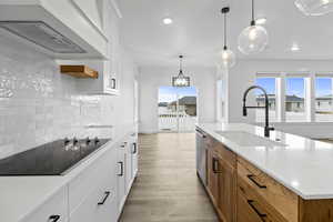 Two tone kitchen with two tone cabinets, pendant lighting, black electric stovetop, a center island with sink, and light wood-type flooring