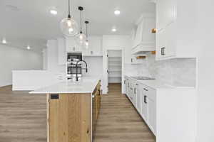Kitchen featuring a center island with sink, dual tone cabinetry, light wood finished floors, hanging light fixtures, and light stone countertops