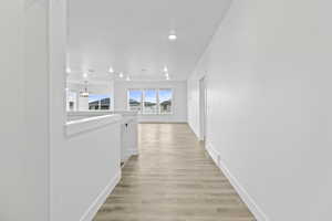 Hallway with light wood finished floors, an upstairs landing, and suspended lighting