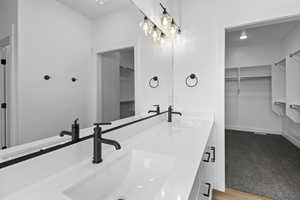 Full bath with a spacious closet, double vanity, light carpet, and light wood-type flooring
