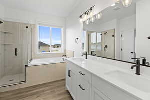 Full bath featuring a shower stall, double vanity, a bath, and light wood-style flooring