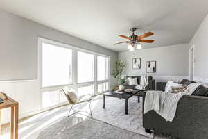 Living area with a wainscoted wall, a ceiling fan, healthy amount of natural light, and carpet floors