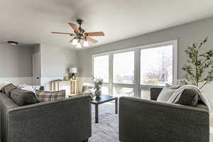 Living area with wainscoting, a ceiling fan, and a decorative wall