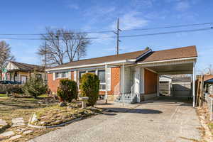 Single story home featuring driveway, an attached carport, brick siding, and a shingled roof