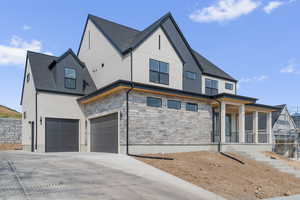 View of front of house featuring stone siding, concrete driveway, a shingled roof, and covered porch