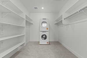 Laundry area featuring light carpet and stacked washer and dryer