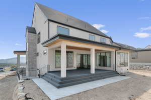Rear view of house with stucco siding, a patio, stone siding, and roof with shingles