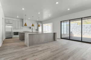 Kitchen featuring a center island with sink, stainless steel appliances, pendant lighting, light stone counters, and light wood-type flooring
