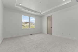 Spare room with a tray ceiling, light colored carpet, and recessed lighting