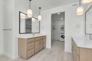 Bathroom with a walk in closet, two vanities, and stacked washing machine and dryer