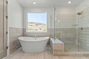 Bathroom featuring a stall shower, a soaking tub, tile walls, and wainscoting
