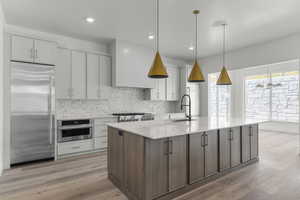 Kitchen with two tone cabinetry, stainless steel appliances, light stone countertops, light wood-type flooring, and pendant lighting