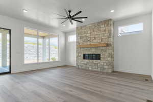 Unfurnished living room with a stone fireplace, a ceiling fan, and wood finished floors