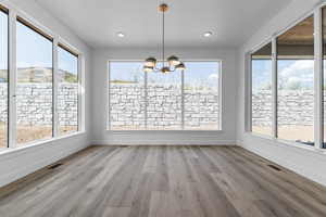 Unfurnished dining area with hanging lights, light wood-type flooring, and healthy amount of natural light