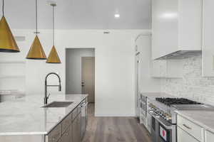 Kitchen featuring high end appliances, an island with sink, dark wood-type flooring, dual tone cabinetry, and light stone counters