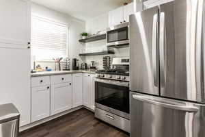 Kitchen with stainless steel appliances, white cabinets, open shelves, and dark wood-type flooring