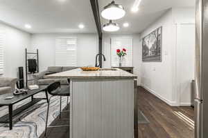 Kitchen with light stone countertops, dark wood-style floors, a center island with sink, hanging light fixtures, and freestanding refrigerator