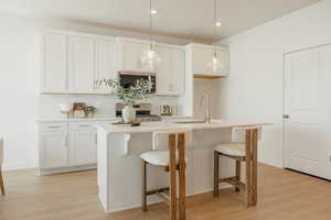 Kitchen with a kitchen island with sink, decorative light fixtures, a breakfast bar, and light wood-type flooring