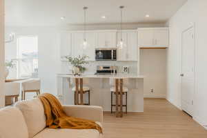 Kitchen featuring a kitchen bar, white cabinetry, light wood finished floors, a kitchen island with sink, and stainless steel appliances