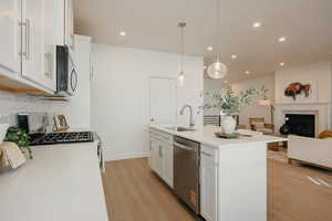 Kitchen featuring white cabinetry, open floor plan, stainless steel appliances, an island with sink, and a glass covered fireplace
