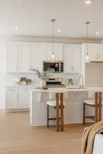 Kitchen featuring a kitchen bar, a kitchen island with sink, white cabinets, and light wood finished floors
