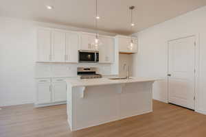 Kitchen with white cabinetry, stainless steel appliances, hanging light fixtures, light wood-style flooring, and a kitchen breakfast bar