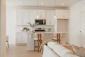 Kitchen featuring decorative light fixtures, white cabinets, a breakfast bar, a center island with sink, and stainless steel appliances