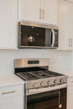 Kitchen with stainless steel appliances, tasteful backsplash, white cabinets, and light stone countertops