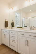 Full bath with double vanity, light wood-style flooring, and a shower stall