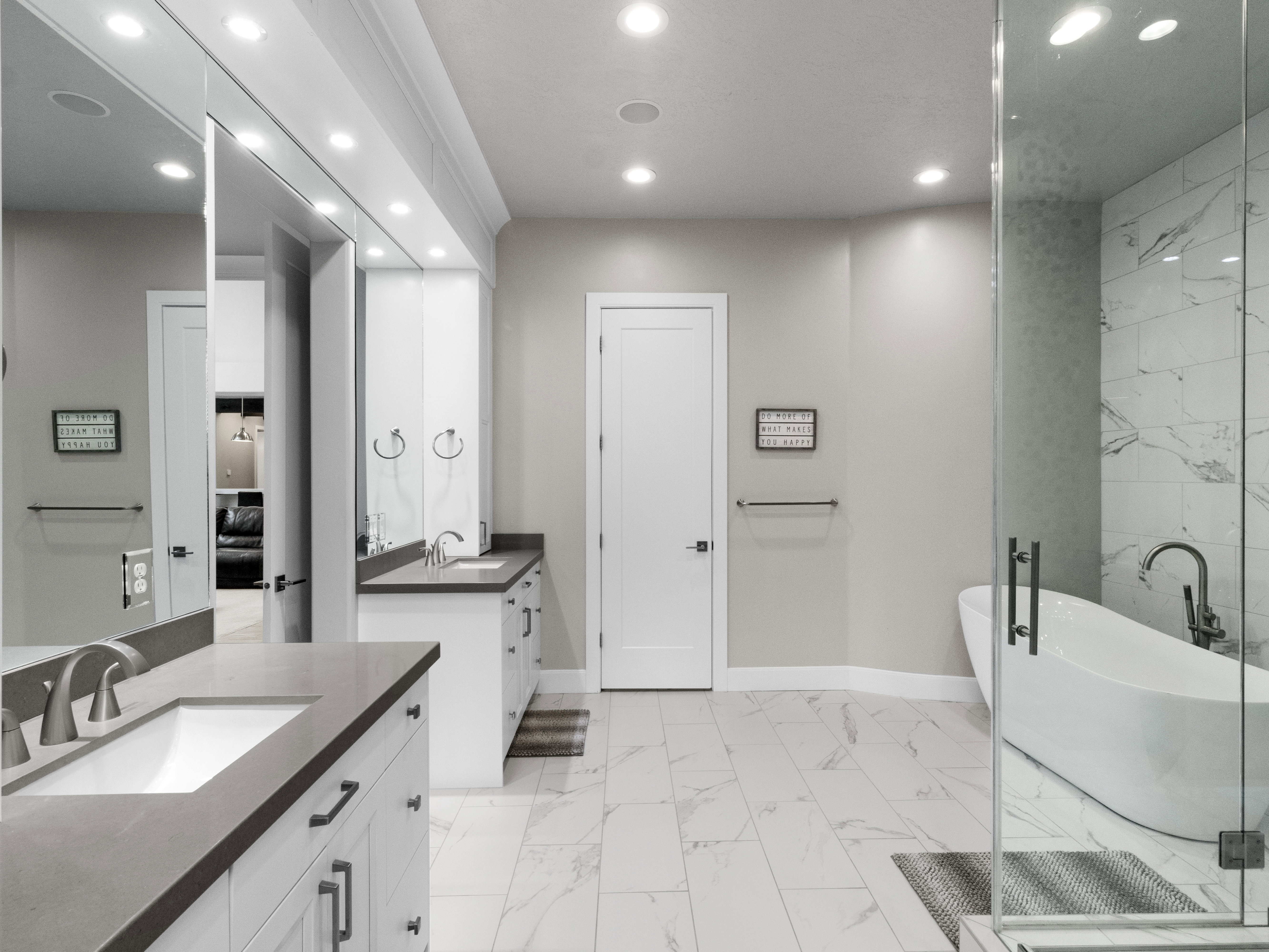 Bathroom with a freestanding bath, recessed lighting, light marble finish flooring, and two vanities