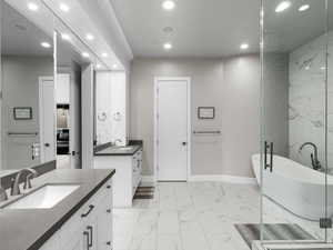 Bathroom with a freestanding bath, recessed lighting, light marble finish flooring, and two vanities
