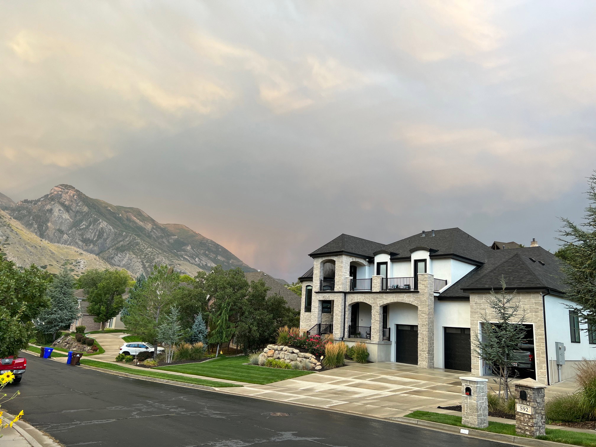 View of front of house with stone siding, concrete driveway, a balcony, a mountain view, and a front yard