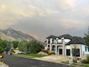 View of front of house with stone siding, concrete driveway, a balcony, a mountain view, and a front yard