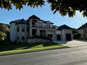 French country inspired facade with stone siding, a balcony, driveway, and a front lawn