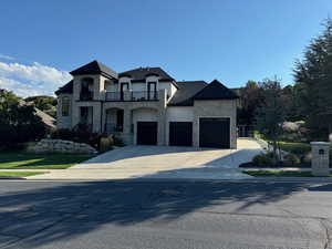 French country home featuring stone siding, a balcony, stucco siding, concrete driveway, and a garage