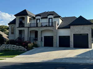 French country home featuring stone siding, stucco siding, concrete driveway, and a balcony