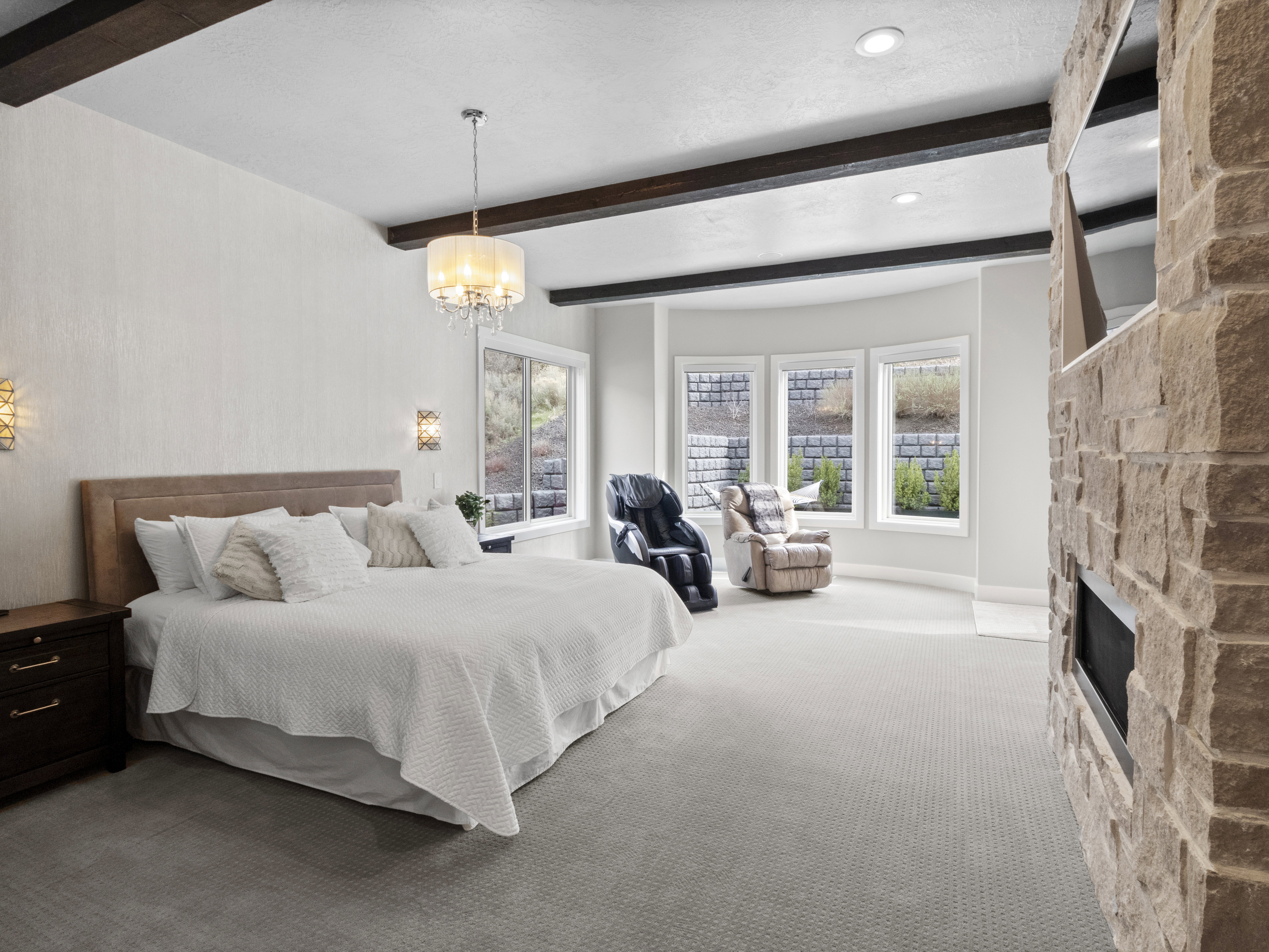 Bedroom with carpet, beamed ceiling, multiple windows, a stone fireplace, and a chandelier