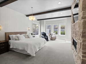 Bedroom with carpet, beamed ceiling, multiple windows, a stone fireplace, and a chandelier