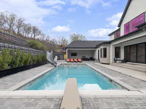 View of swimming pool with a water slide, patio surround, a fenced backyard, a diving board, and outdoor seating