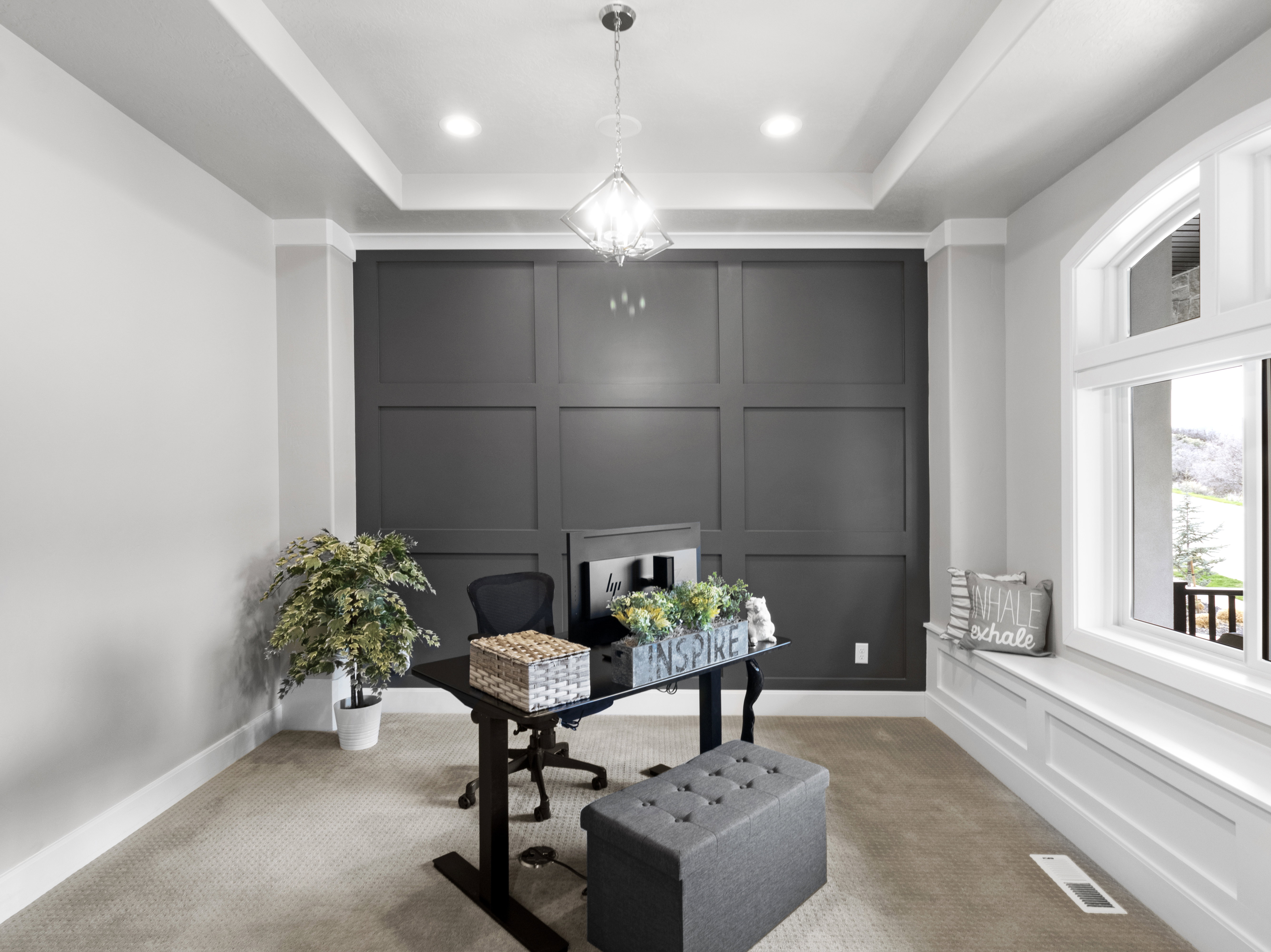 Carpeted office space featuring a decorative wall, a raised ceiling, and suspended lighting