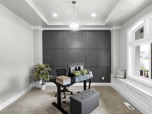 Carpeted office space featuring a decorative wall, a raised ceiling, and suspended lighting