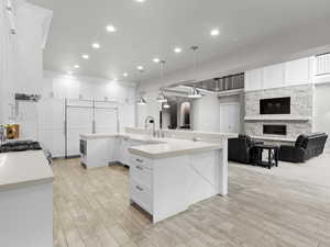 Kitchen with a stone fireplace, open floor plan, white cabinets, light wood-style floors, and hanging light fixtures