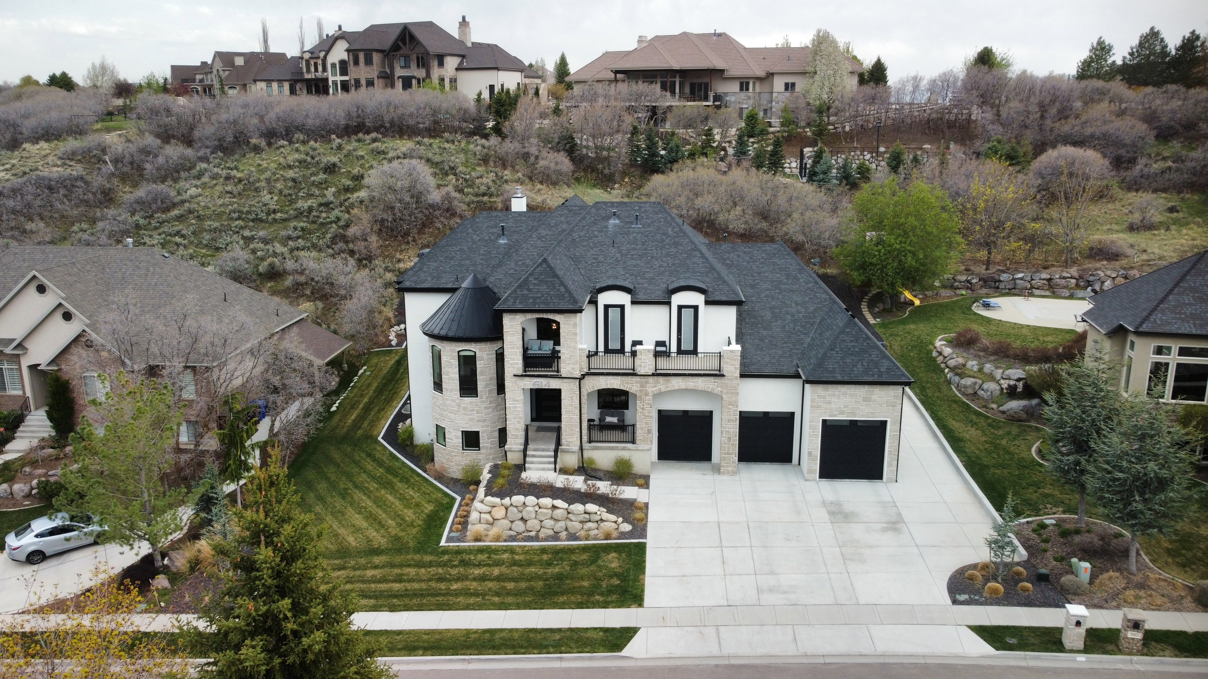 French provincial home with stone siding, a residential view, concrete driveway, a balcony, and a chimney