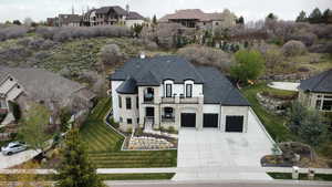 French provincial home with stone siding, a residential view, concrete driveway, a balcony, and a chimney