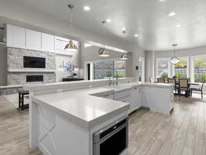 Kitchen featuring white cabinets, decorative light fixtures, light wood-style floors, a fireplace, and open floor plan