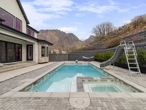 Relaxing pool / spa featuring a patio area, a fenced backyard, a water slide, and a mountain view