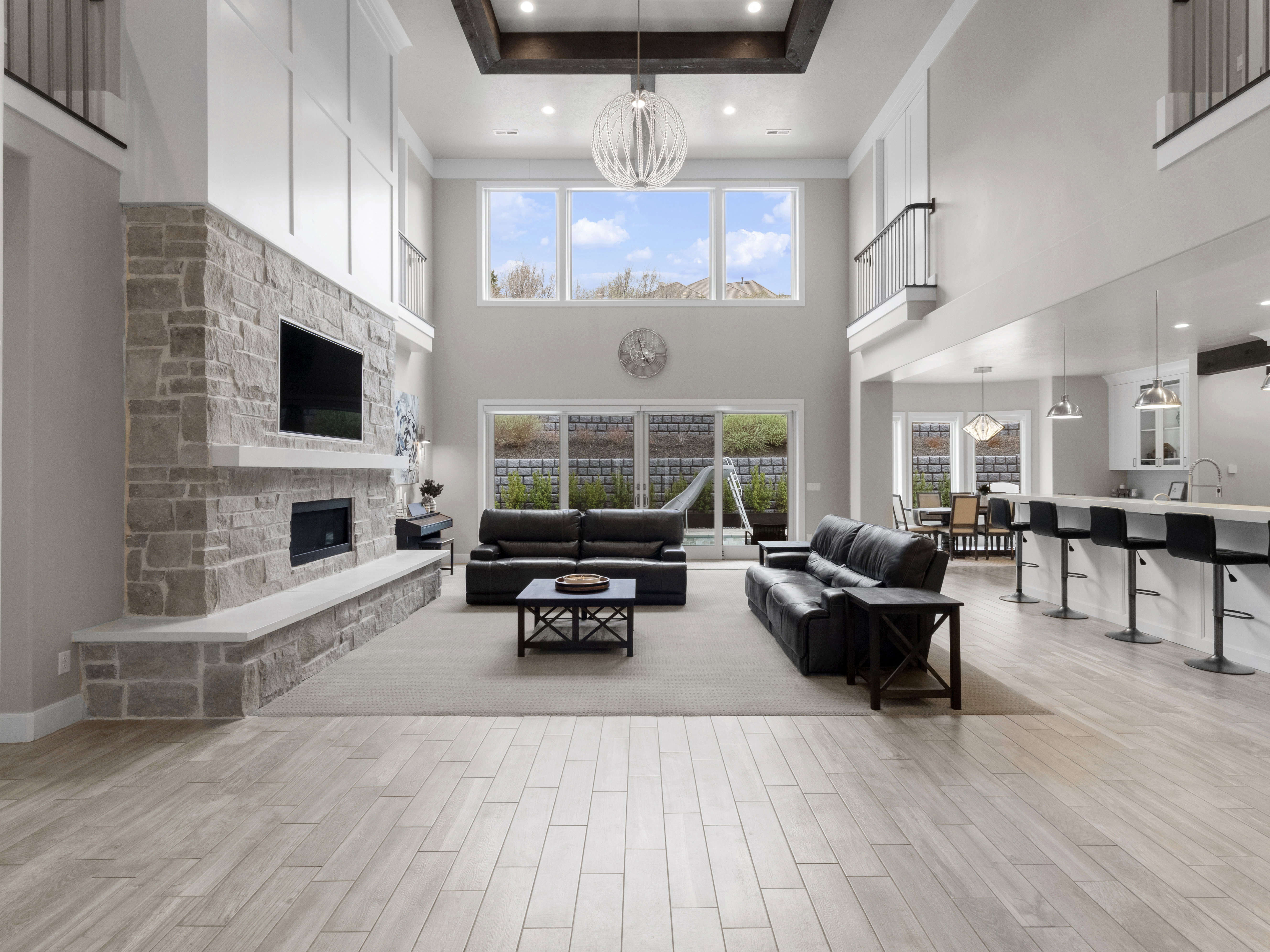 Living room with a stone fireplace, wood tiled floors, a chandelier, and a high tray ceiling