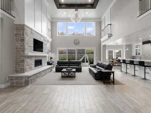 Living room with a stone fireplace, wood tiled floors, a chandelier, and a high tray ceiling