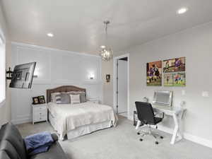 Carpeted bedroom featuring a decorative wall, a desk, and suspended lighting
